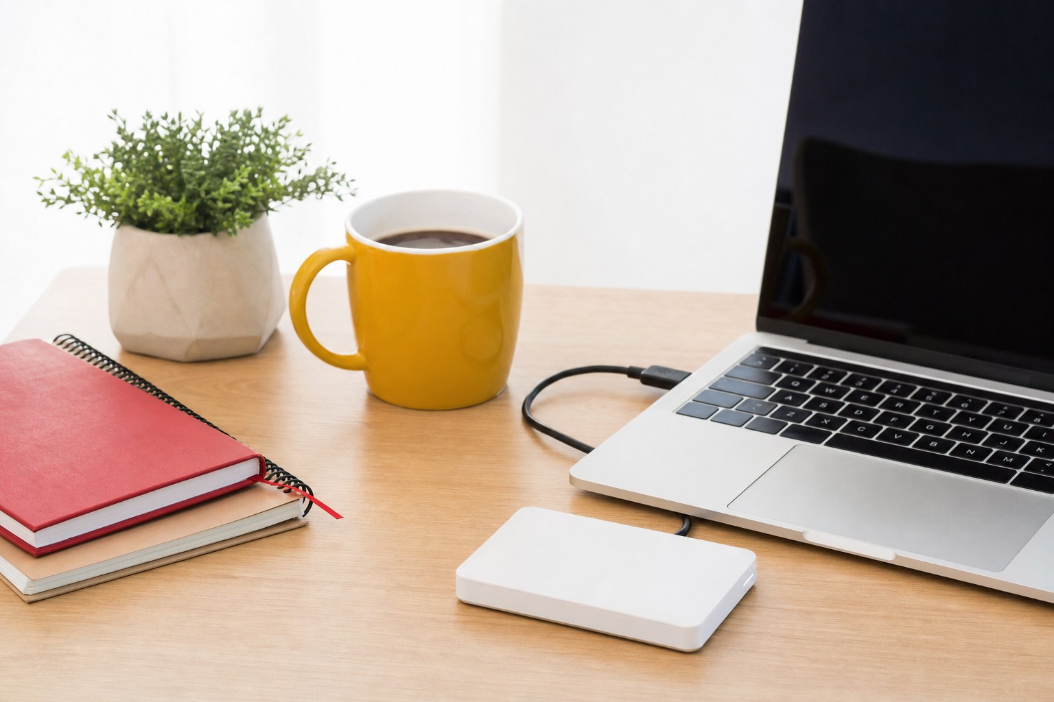 Disque dur externe blanc branché à un ordinateur portable sur un bureau en bois clair, illustration de l'importance des sauvegardes régulières des données professionnelles contre les cyberattaques