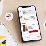 Un smartphone posé sur un bureau en bois affiche une conversation avec un assistant IA : sous la réponse générée apparaît une carte publicitaire clairement étiquetée sponsorisée, illustration du fonctionnement de ChatGPT Ads pour les annonceurs français.